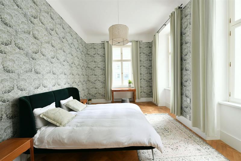 Bedroom with green velvet bed and vintage rug on herringbone parquet