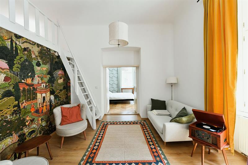 Living room with garden mural, white staircase to mezzanine and view into the bedroom